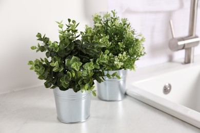 Photo of Artificial potted herbs on white marble countertop near sink in kitchen. Home decor