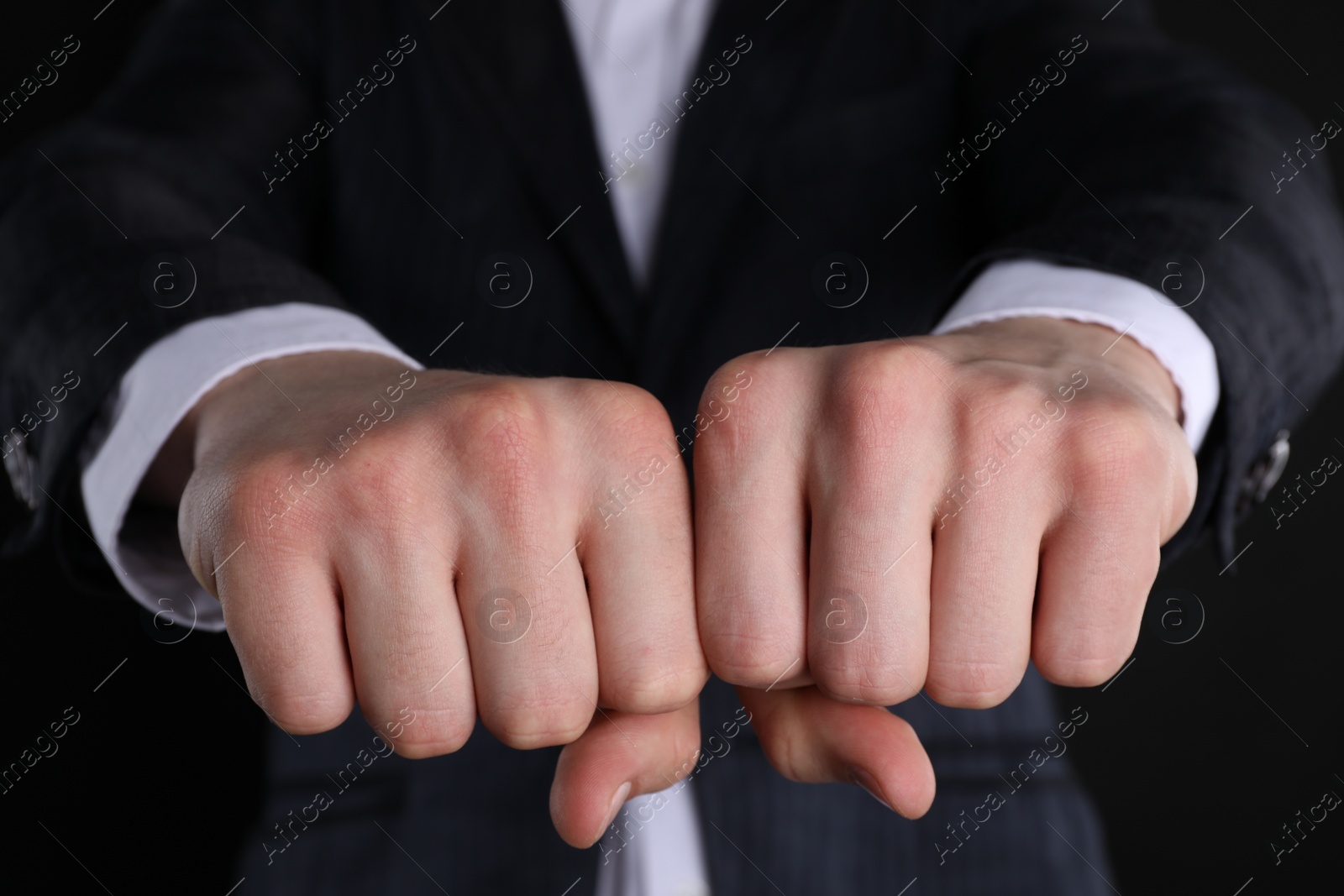 Photo of Businessman showing fists with space for tattoo on black background, closeup