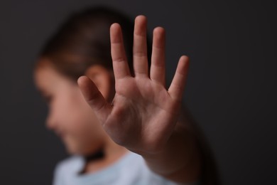 Photo of Child abuse. Little girl doing stop gesture on dark background, selective focus