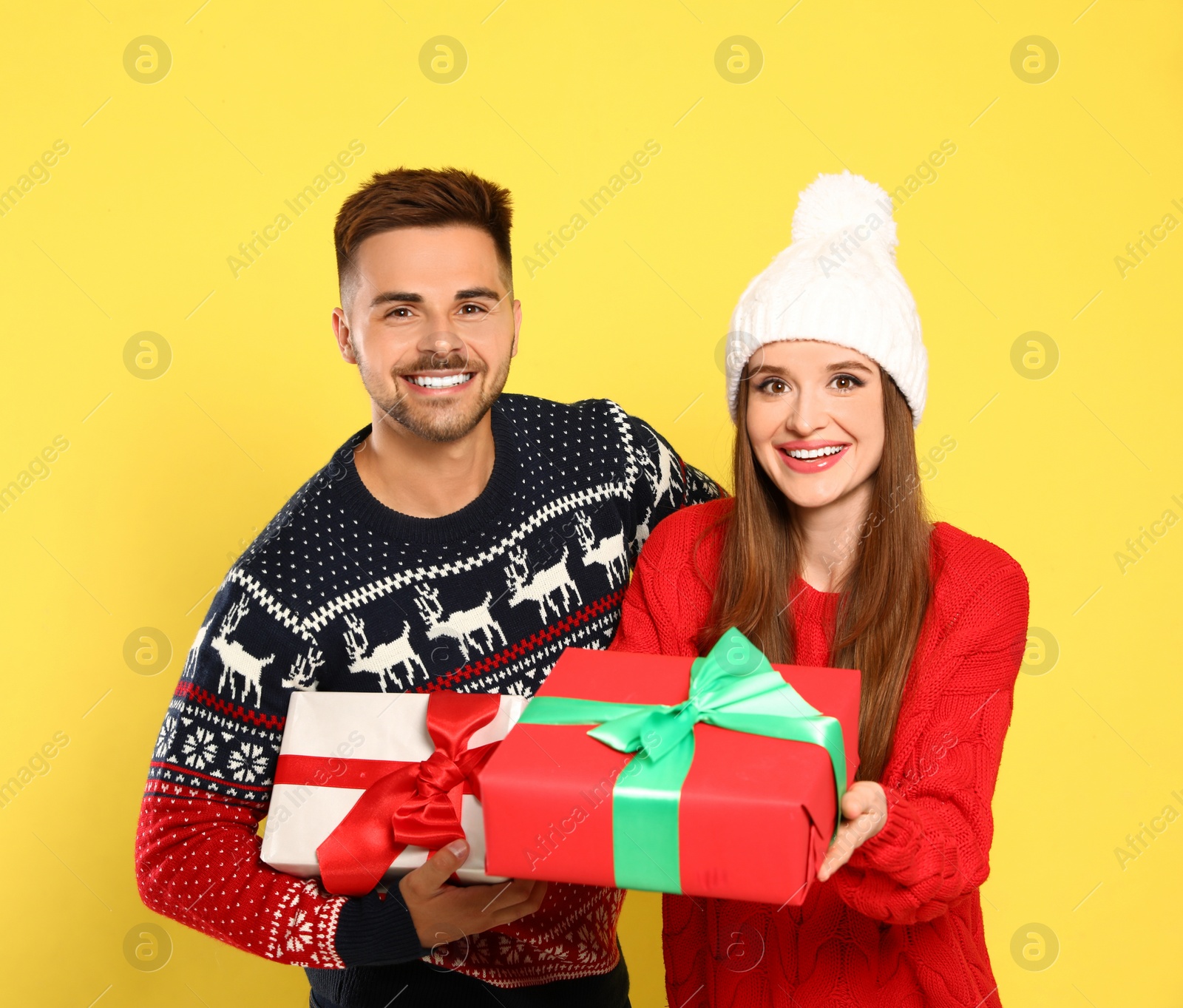 Photo of Couple in Christmas sweaters with gift boxes on yellow background