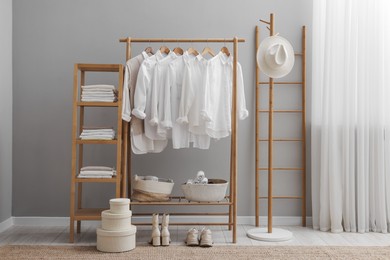 Photo of Wardrobe organization. Rack with different stylish clothes, boxes and shelving unit near grey wall indoors