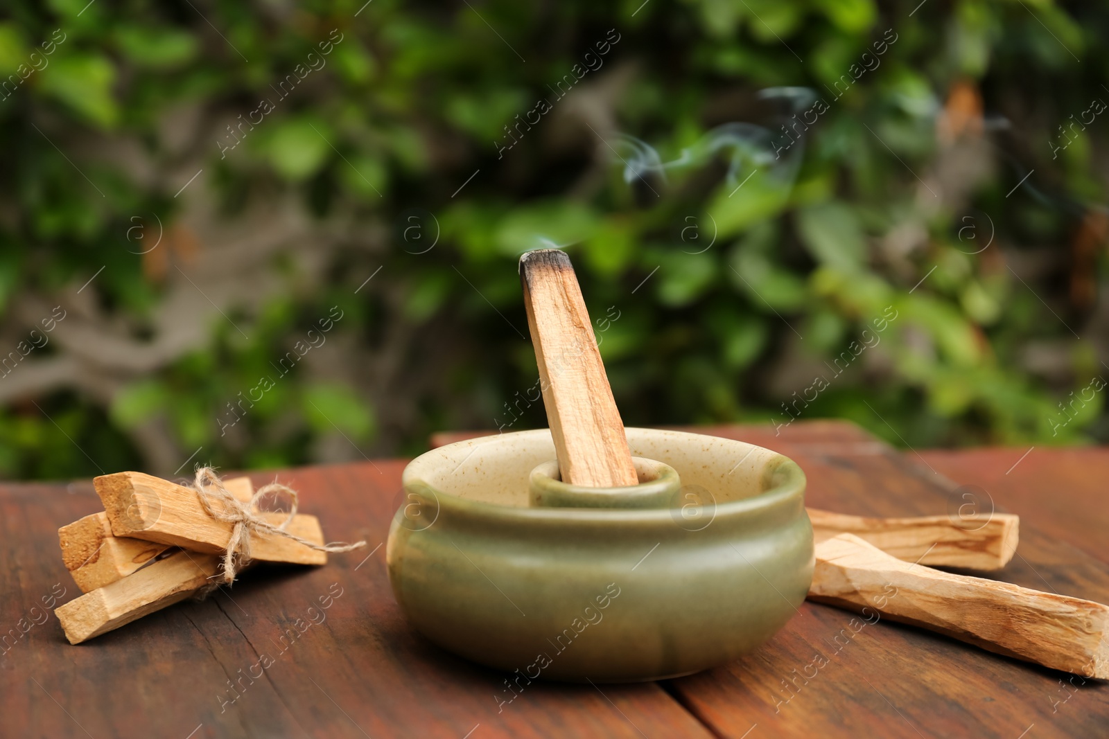 Photo of Palo Santo stick smoldering in holder on wooden table outdoors