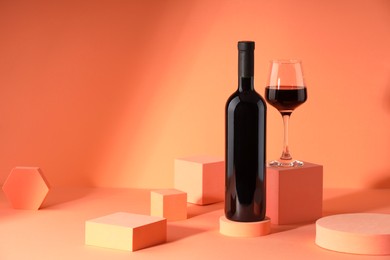 Photo of Stylish presentation of delicious red wine in bottle and glass on orange background. Space for text