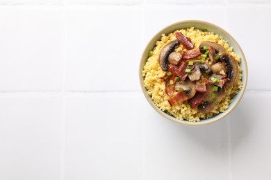 Photo of Tasty millet porridge with mushrooms, bacon and green onion in bowl on white tiled table, top view. Space for text