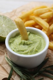 Photo of Delicious french fries, avocado dip, lime and rosemary on parchment