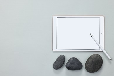 Photo of Modern tablet, stylus and pebbles on light grey background, flat lay. Space for text