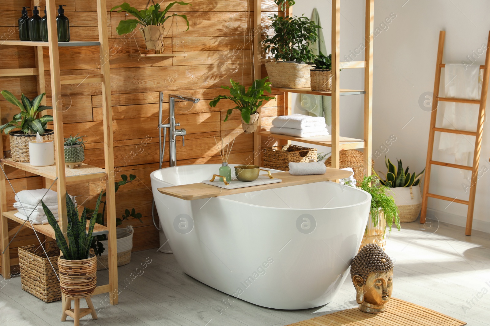 Photo of Stylish bathroom interior with white tub and green houseplants near wooden wall. Idea for design