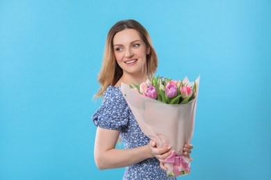 Photo of Happy young woman with bouquet of beautiful tulips on light blue background