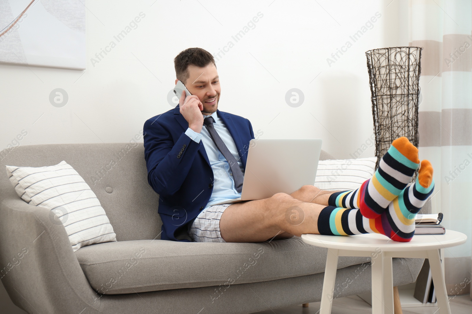 Photo of Businessman in shirt, underwear and funny socks talking on phone during video call at home