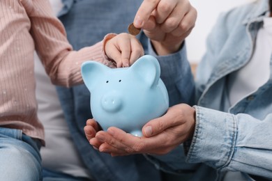 Family budget. Little girl and her parents putting coins into piggy bank, closeup