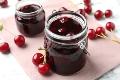 Jars of pickled cherries and fresh fruits on table, closeup