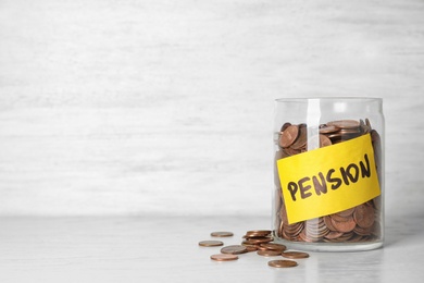 Photo of Coins in glass jar with label "PENSION" on table against light wall. Space for text