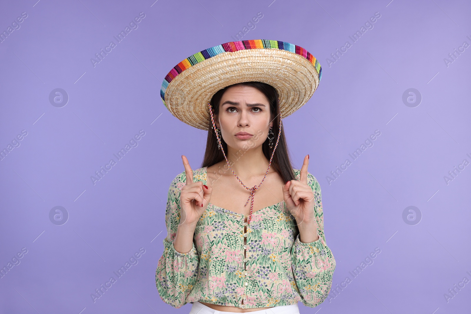 Photo of Young woman in Mexican sombrero hat pointing at something on violet background