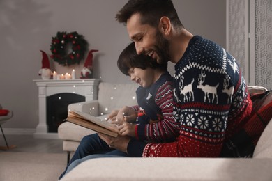 Image of Father with his cute son reading book in room decorated for Christmas
