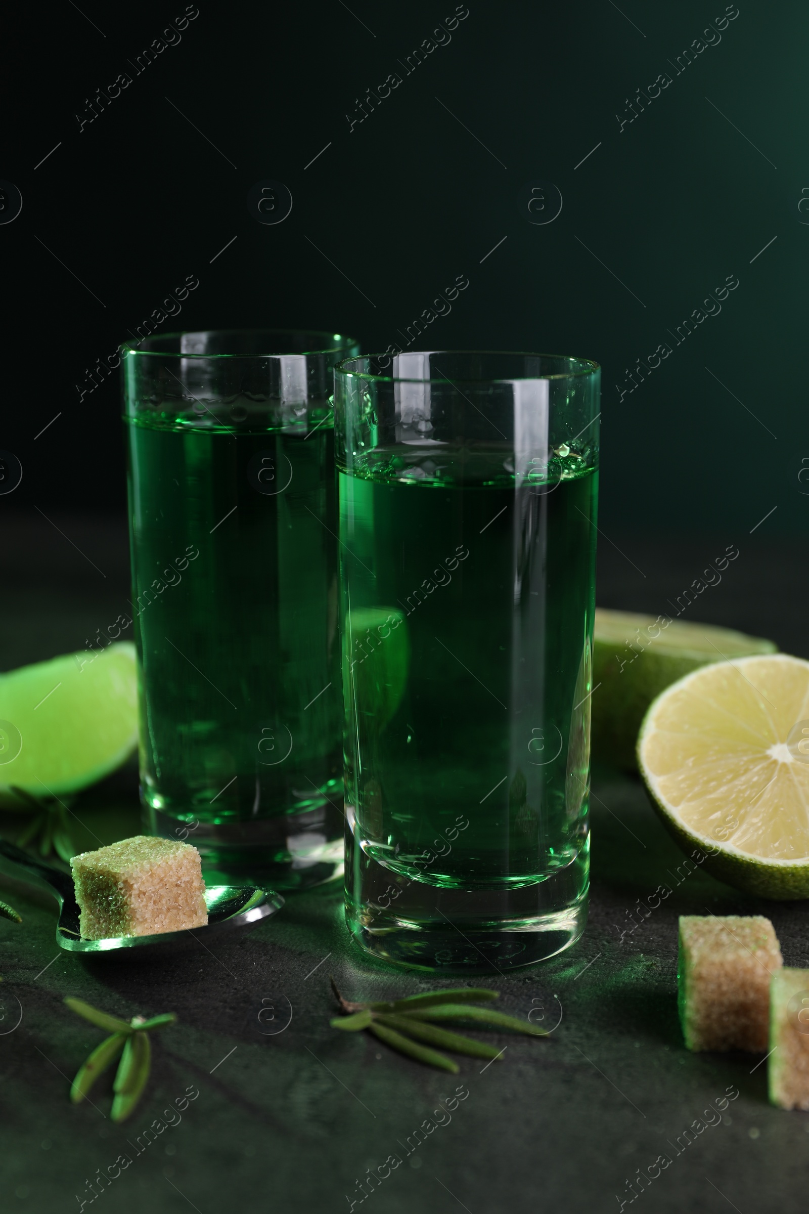 Photo of Absinthe in shot glasses, spoon, brown sugar, lime and rosemary on gray table. Alcoholic drink