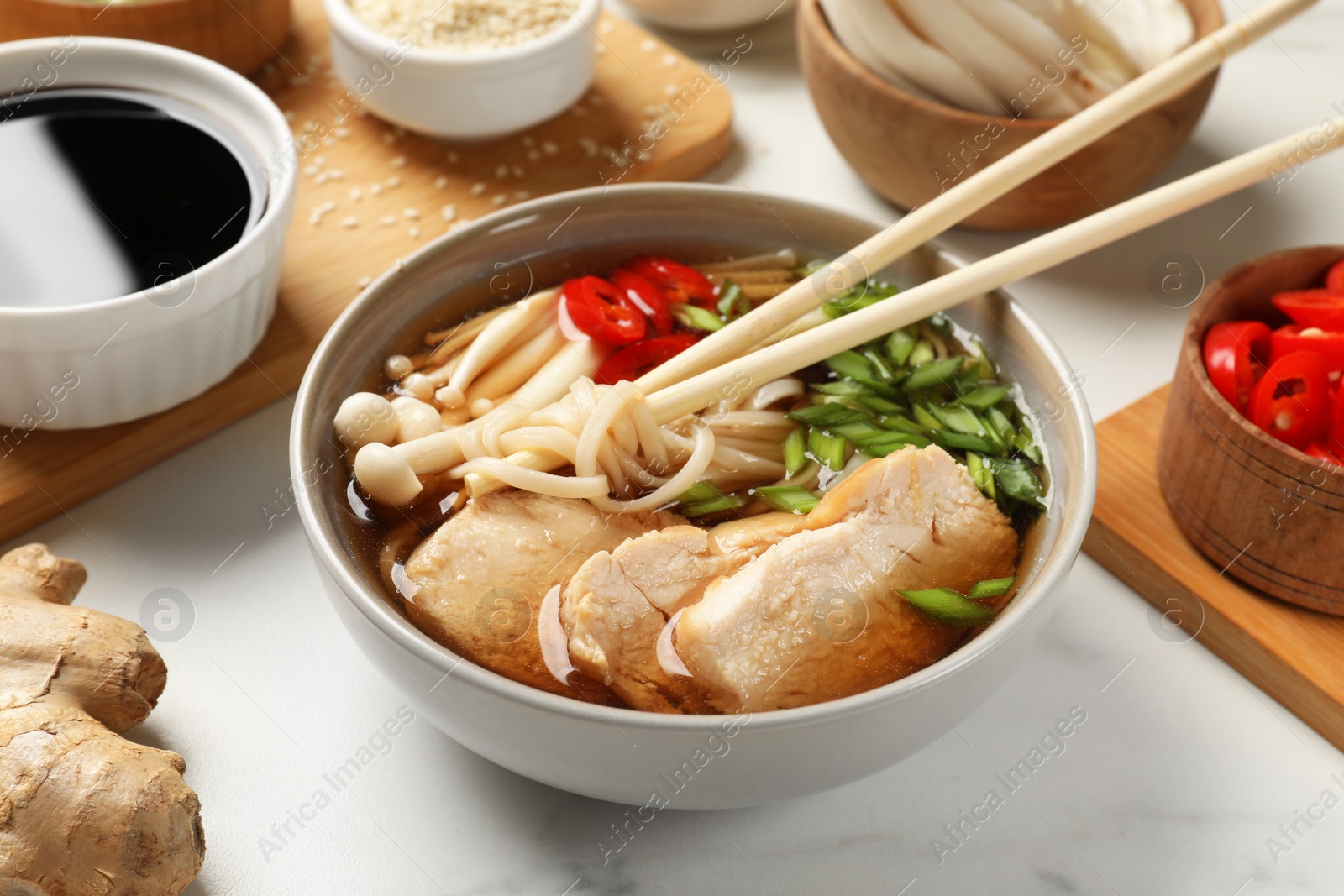 Photo of Delicious ramen with meat and ingredients on white marble table. Noodle soup