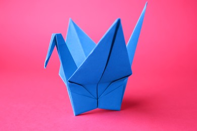 Origami art. Handmade paper crane on pink background, closeup