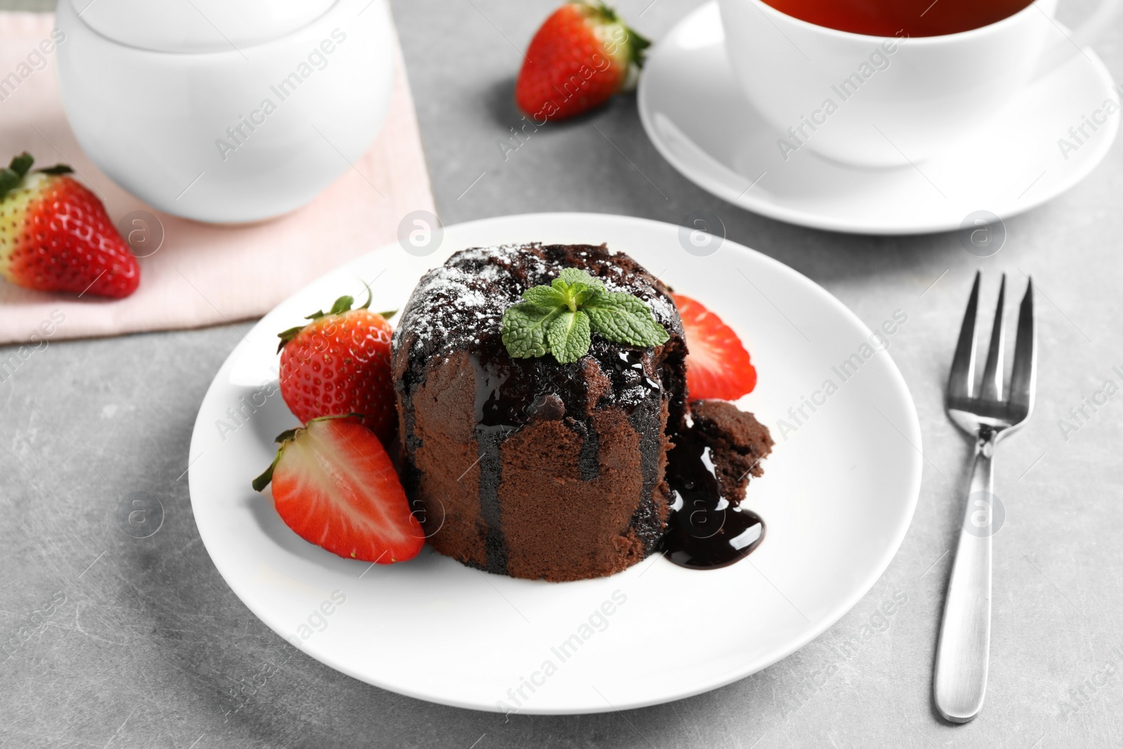 Photo of Delicious warm chocolate lava cake with mint and strawberries on table