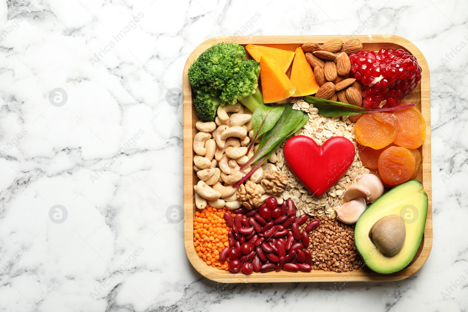 Photo of Wooden tray with heart-healthy products on marble background, top view. Space for text