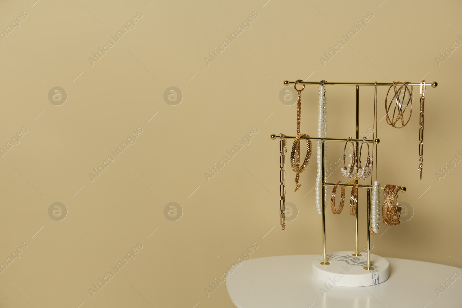 Photo of Holder with set of luxurious jewelry on white table near beige wall, space for text