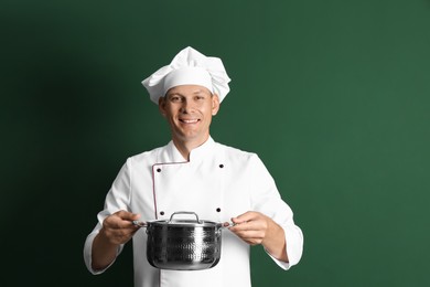 Photo of Happy male chef with cooking pot on dark green background