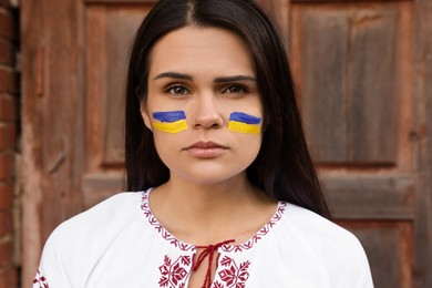 Young beautiful woman with drawings of Ukrainian flag on face near wooden door