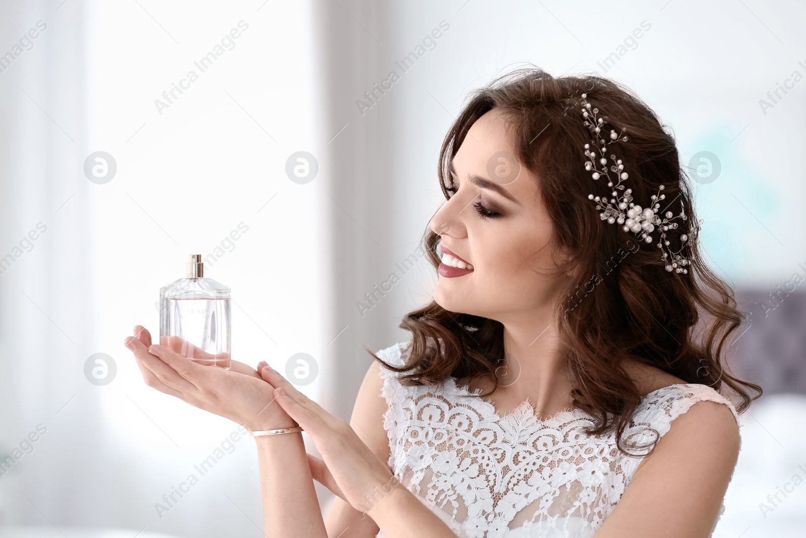 Photo of Beautiful young bride with bottle of perfume on blurred background