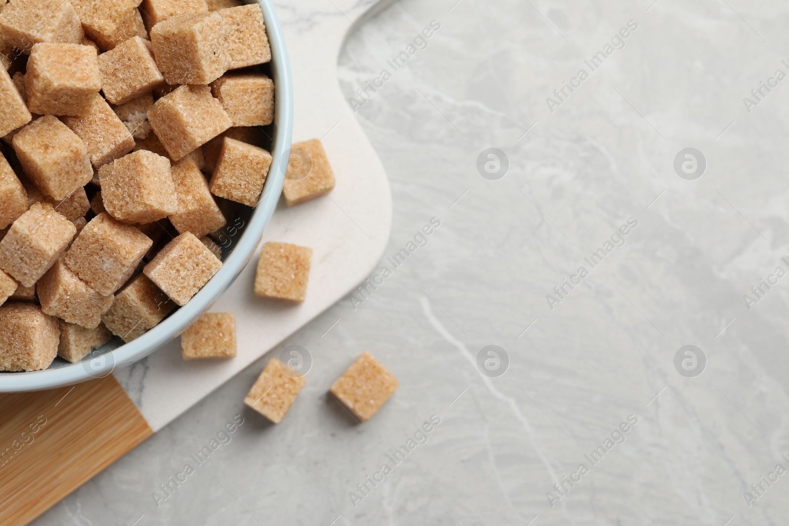 Photo of Bowl of brown sugar cubes on light grey marble table, top view. Space for text