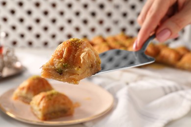 Photo of Woman serving delicious sweet baklava at table, closeup