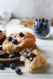 Delicious croissant with chocolate and blueberries on white wooden table, closeup