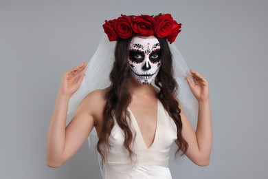 Photo of Young woman in scary bride costume with sugar skull makeup and flower crown on light grey background. Halloween celebration