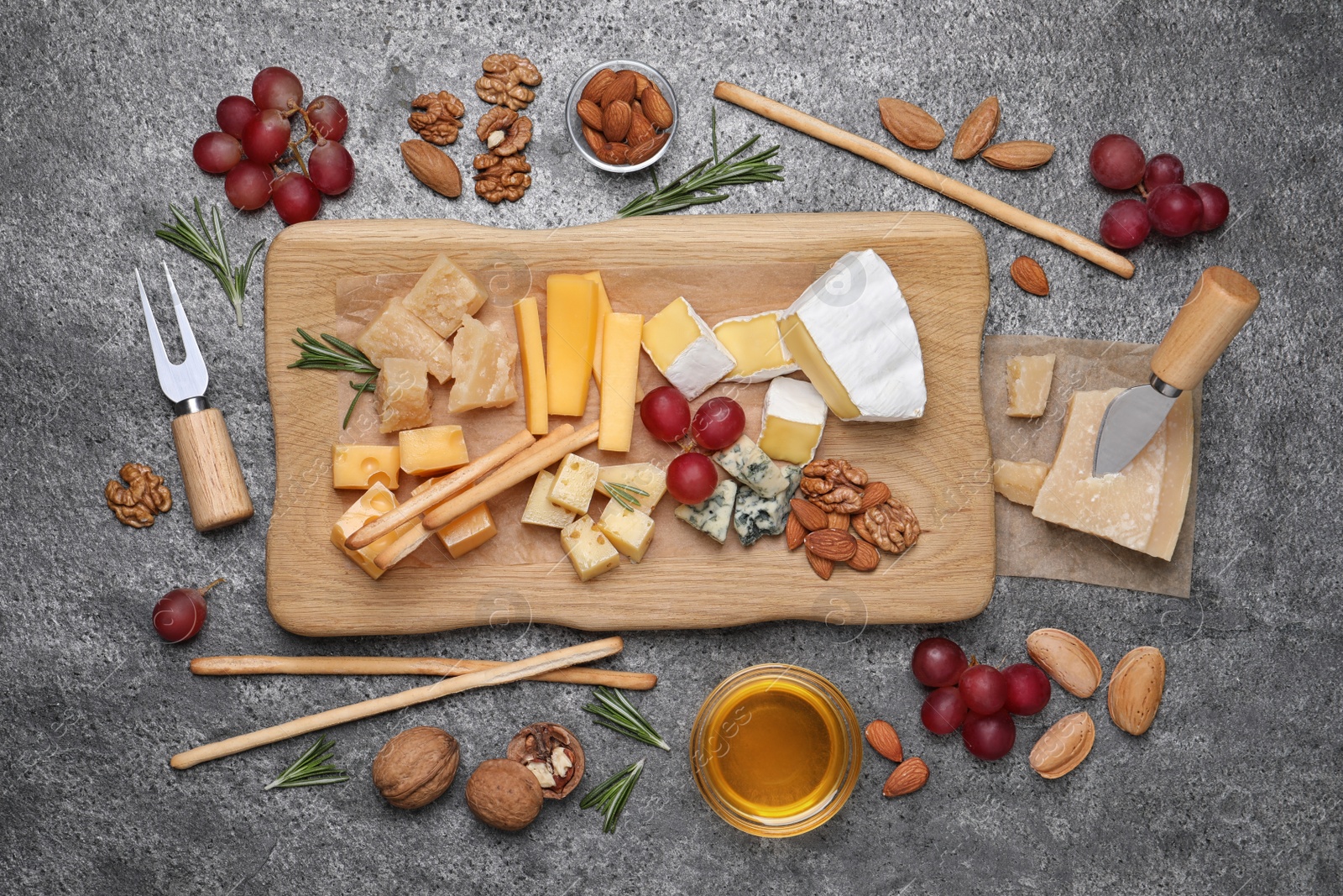 Photo of Cheese plate with honey, grapes and nuts on grey table, flat lay