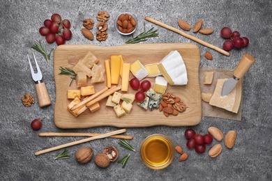 Cheese plate with honey, grapes and nuts on grey table, flat lay