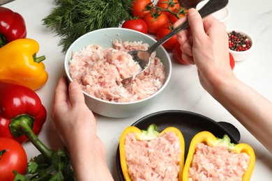 Photo of Woman making stuffed peppers with ground meat at white table, closeup