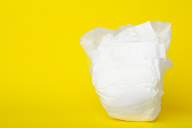 Photo of Baby diaper on yellow background, closeup. Space for text