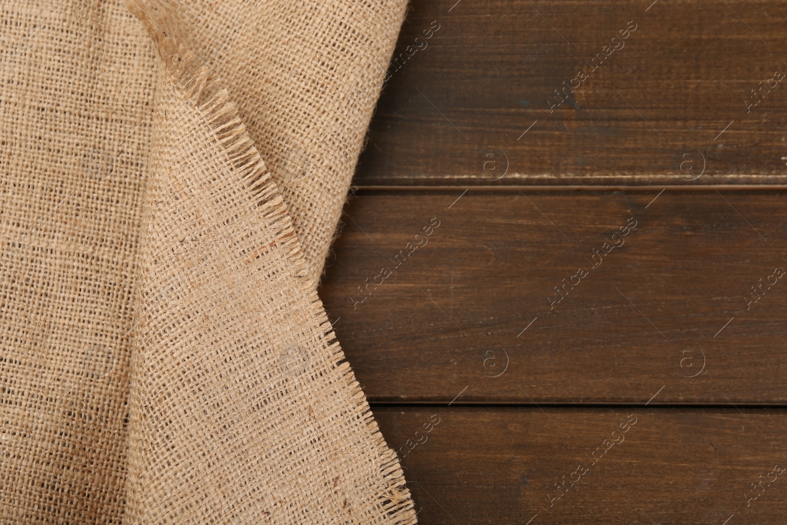Photo of Brown burlap fabric on wooden table, top view. Space for text