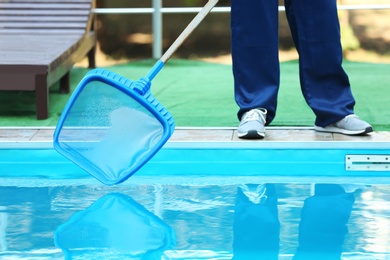 Photo of Male worker cleaning outdoor pool with scoop net