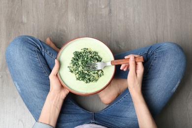 Young woman with tasty cooked spinach on wooden floor, top view. Healthy food