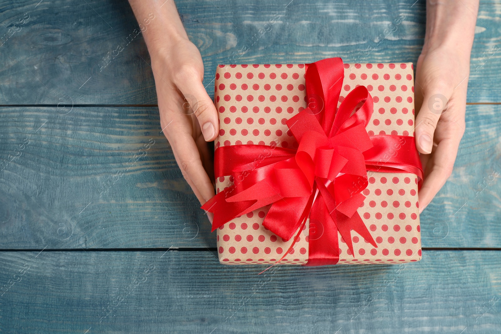 Photo of Young woman holding beautiful gift box on wooden background, top view