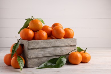 Delicious tangerines with leaves on light wooden table. Space for text