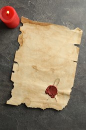 Sheet of old parchment paper with wax stamp and candle on grey table, top view