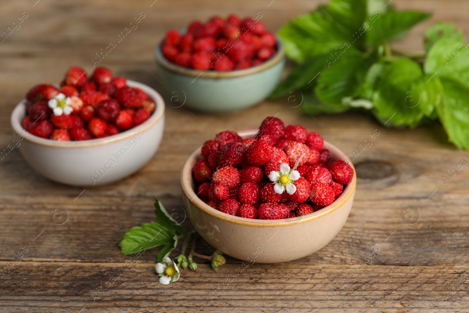 Photo of Fresh wild strawberries and flowers in bowls on wooden table