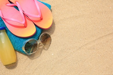 Photo of Stylish sunglasses, flip flops. towel and bottle of refreshing drink on sand, above view. Space for text