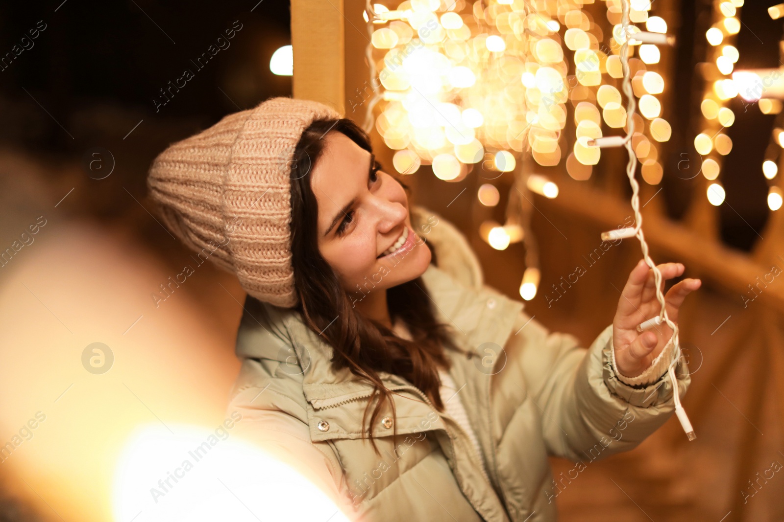 Photo of Beautiful young woman near festive lights outdoors. Winter vacation