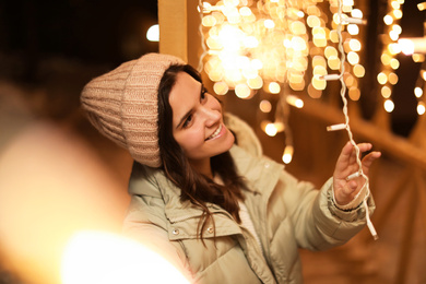 Beautiful young woman near festive lights outdoors. Winter vacation