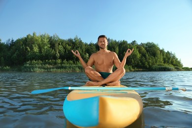 Photo of Man meditating on color SUP board on river