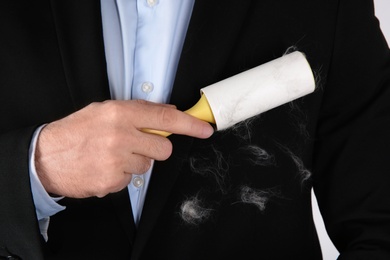 Photo of Man removing hair from black jacket with lint roller, closeup