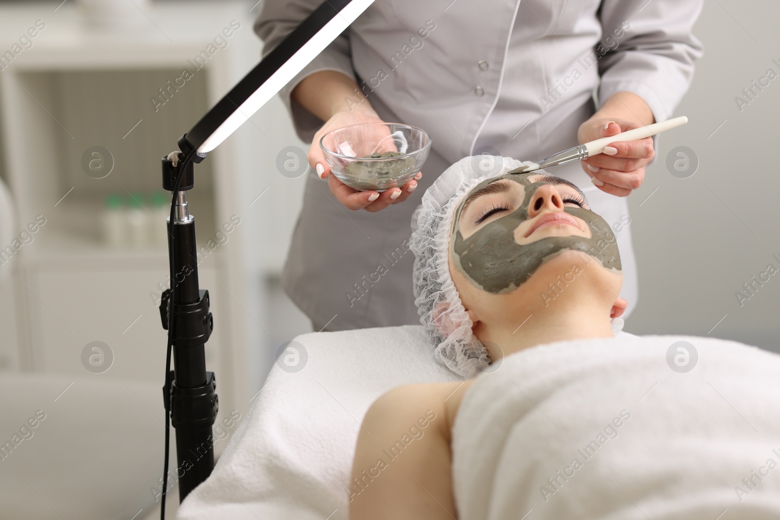 Photo of Cosmetologist applying mask on woman's face in clinic, closeup