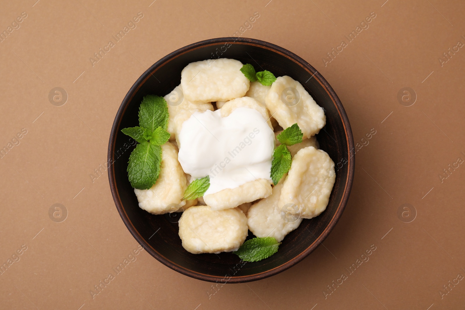 Photo of Bowl of tasty lazy dumplings with sour cream and mint leaves on light brown background, top view