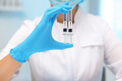 Doctor holding syringes with COVID-19 vaccine on blurred background, closeup